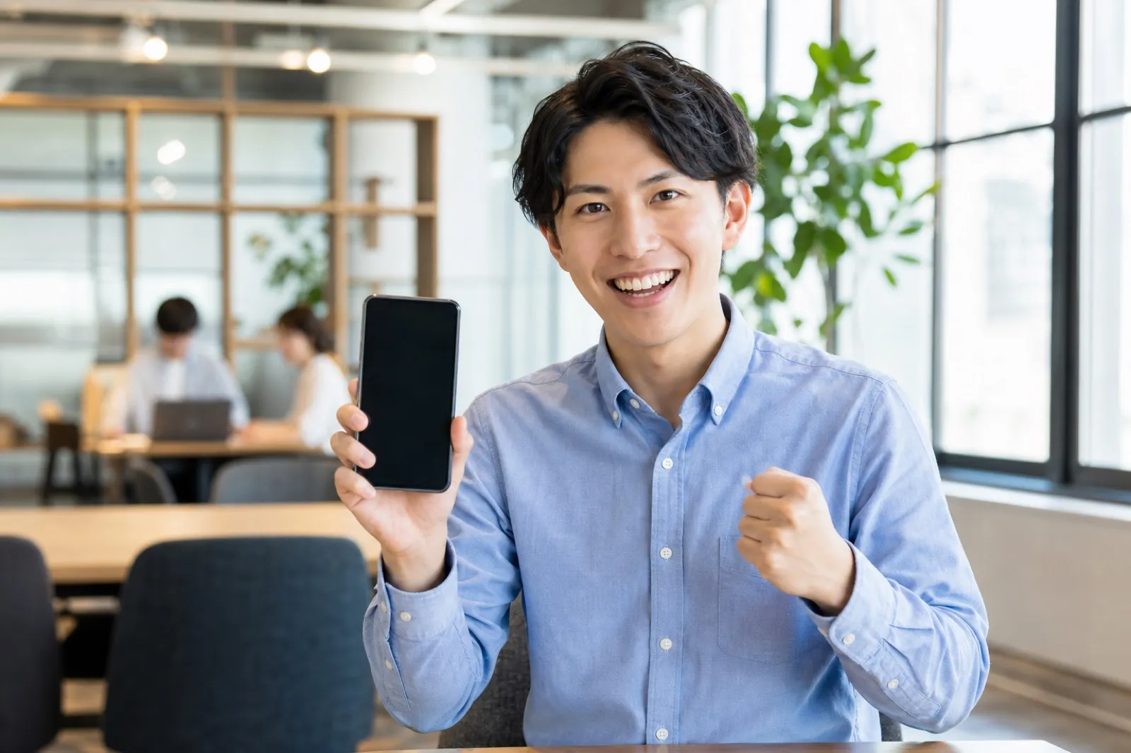 スマートフォンを手に笑顔の若いビジネスパーソン(2023年のAI熱狂のイメージ)